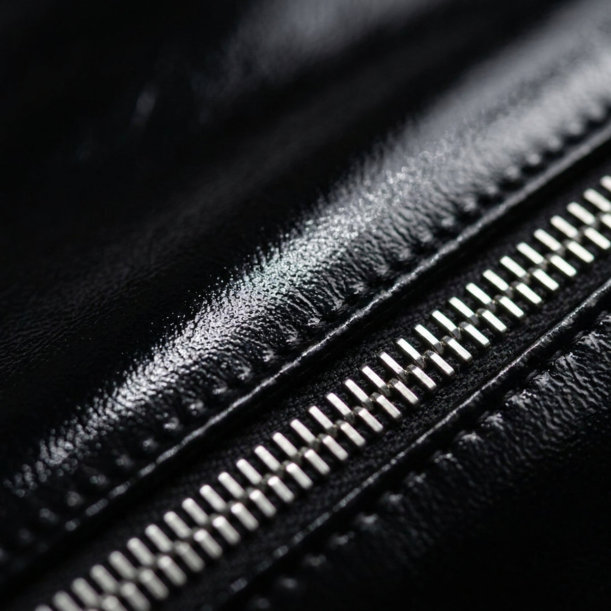 Macro du cuir verni noir de LUCIEN : le laquage posé sur un grain marqué, et les maillons argentés de la glissière.