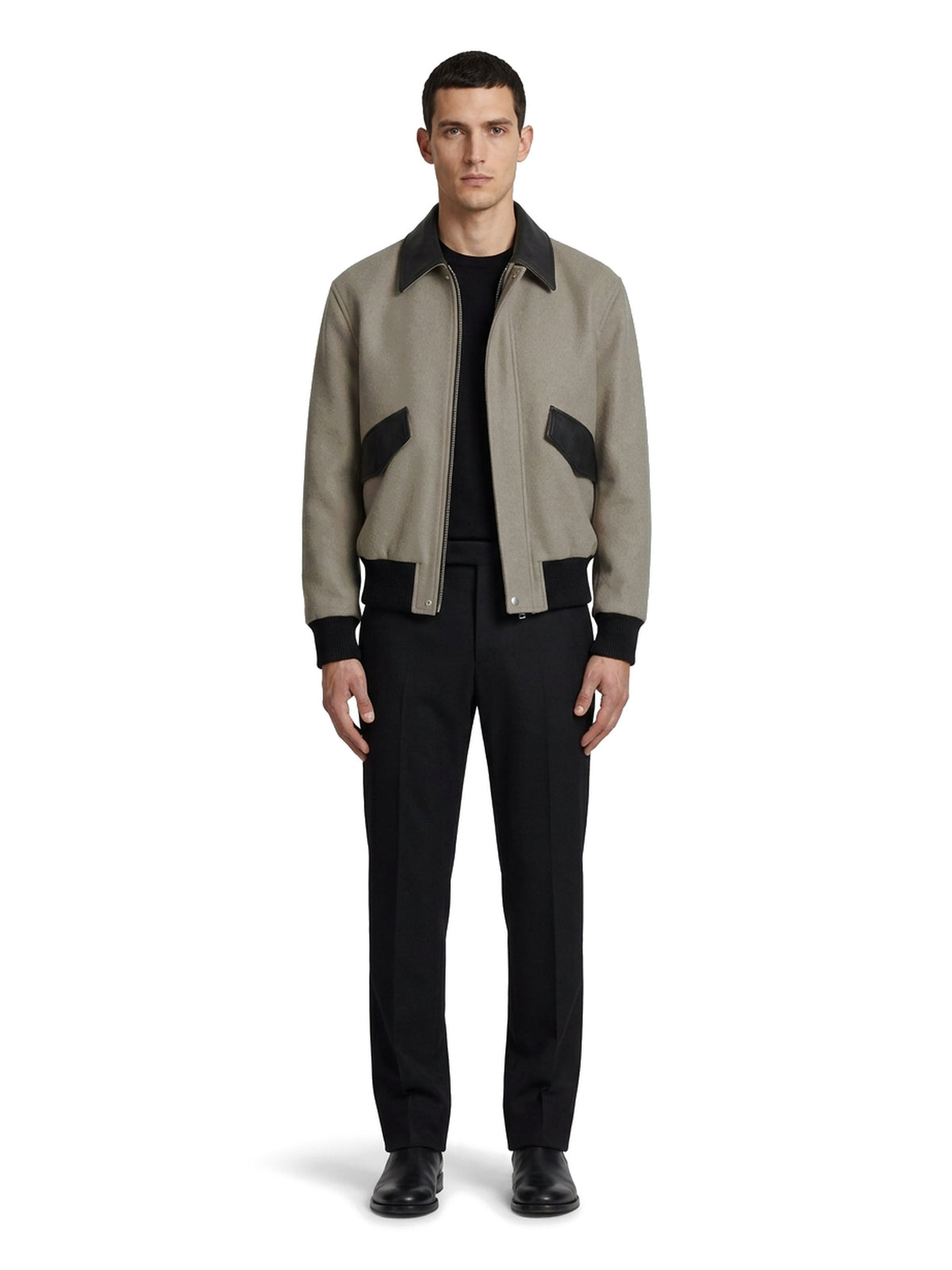 HENRI, blouson en lainage greige à col espagnol de cuir d'agneau noir, vu de face, porté ouvert sur un col rond noir et un pantalon noir.