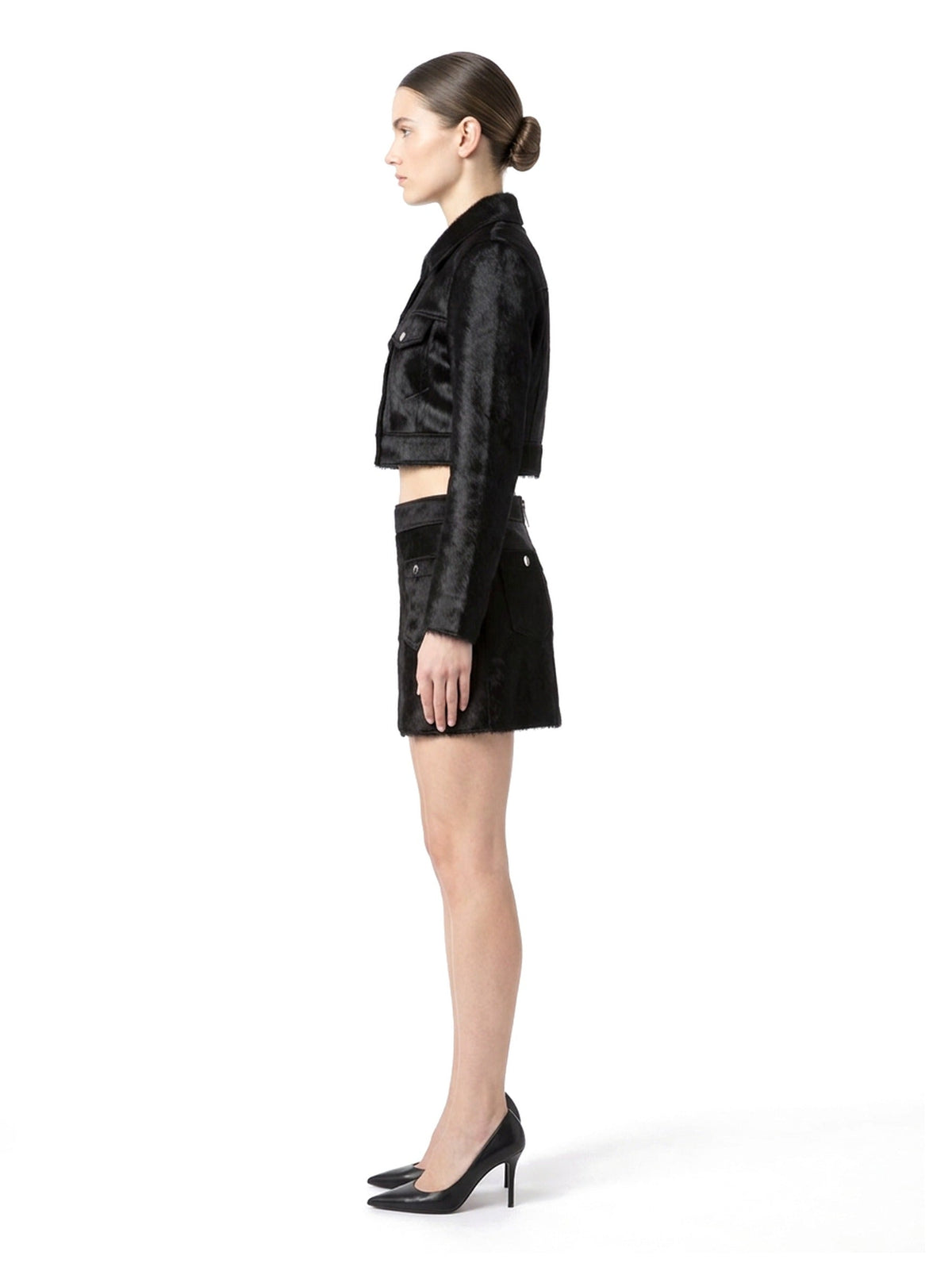 Jupe courte en poil de veau à ras noir, portée avec la veste assortie, vue de profil.