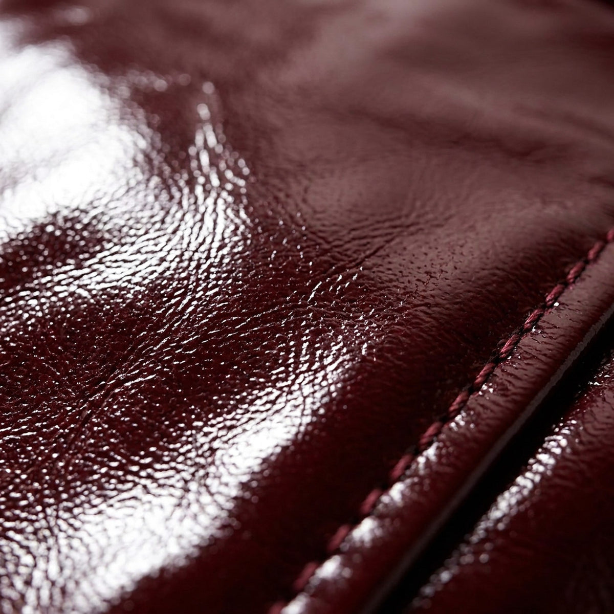 Macro du cuir verni bordeaux et d'un bouton doré, jupe RADICE Maison Godefroi